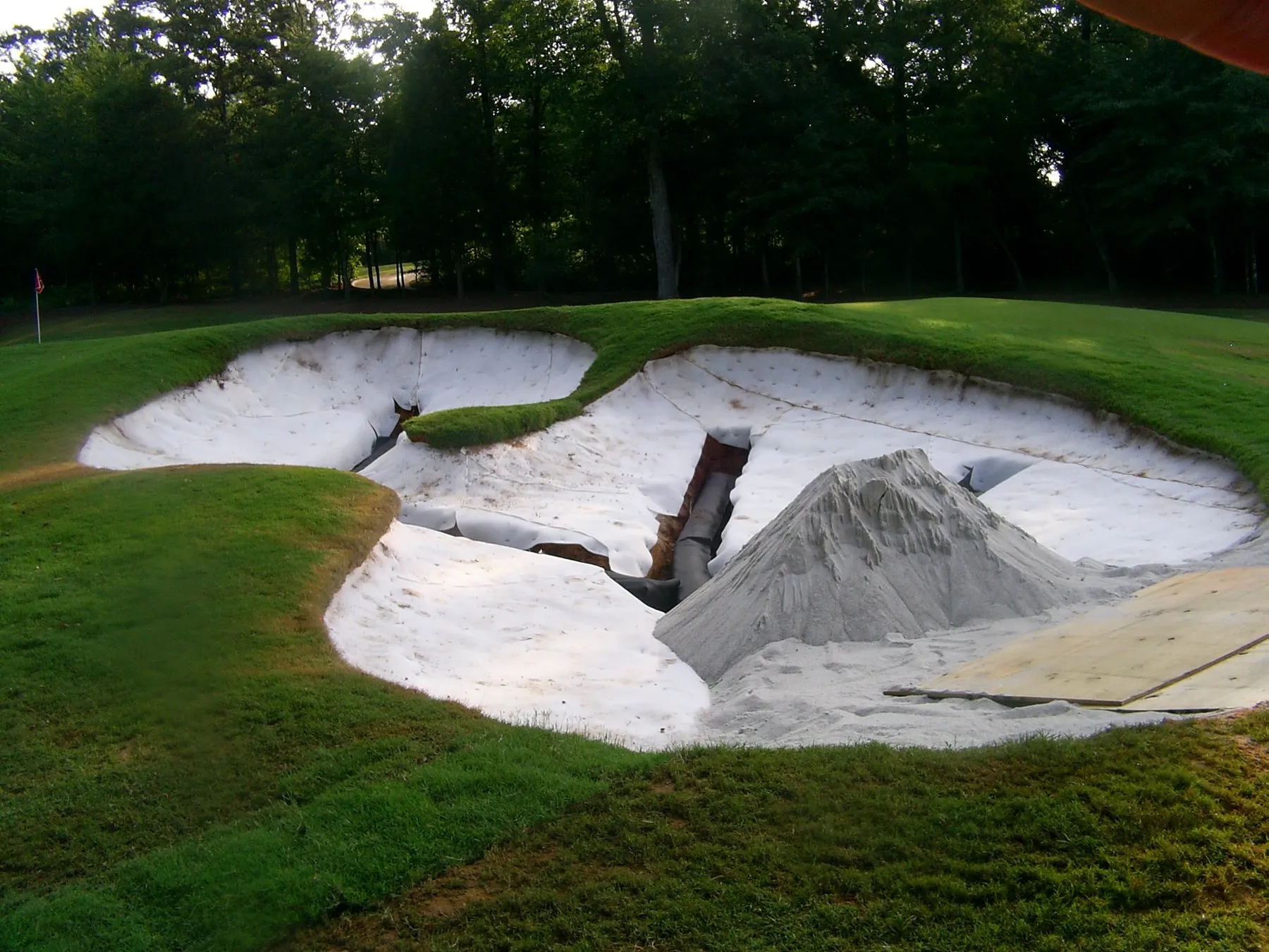 A bunker under construction, liner laid in the base and a mound of fresh sand waiting to be spread.