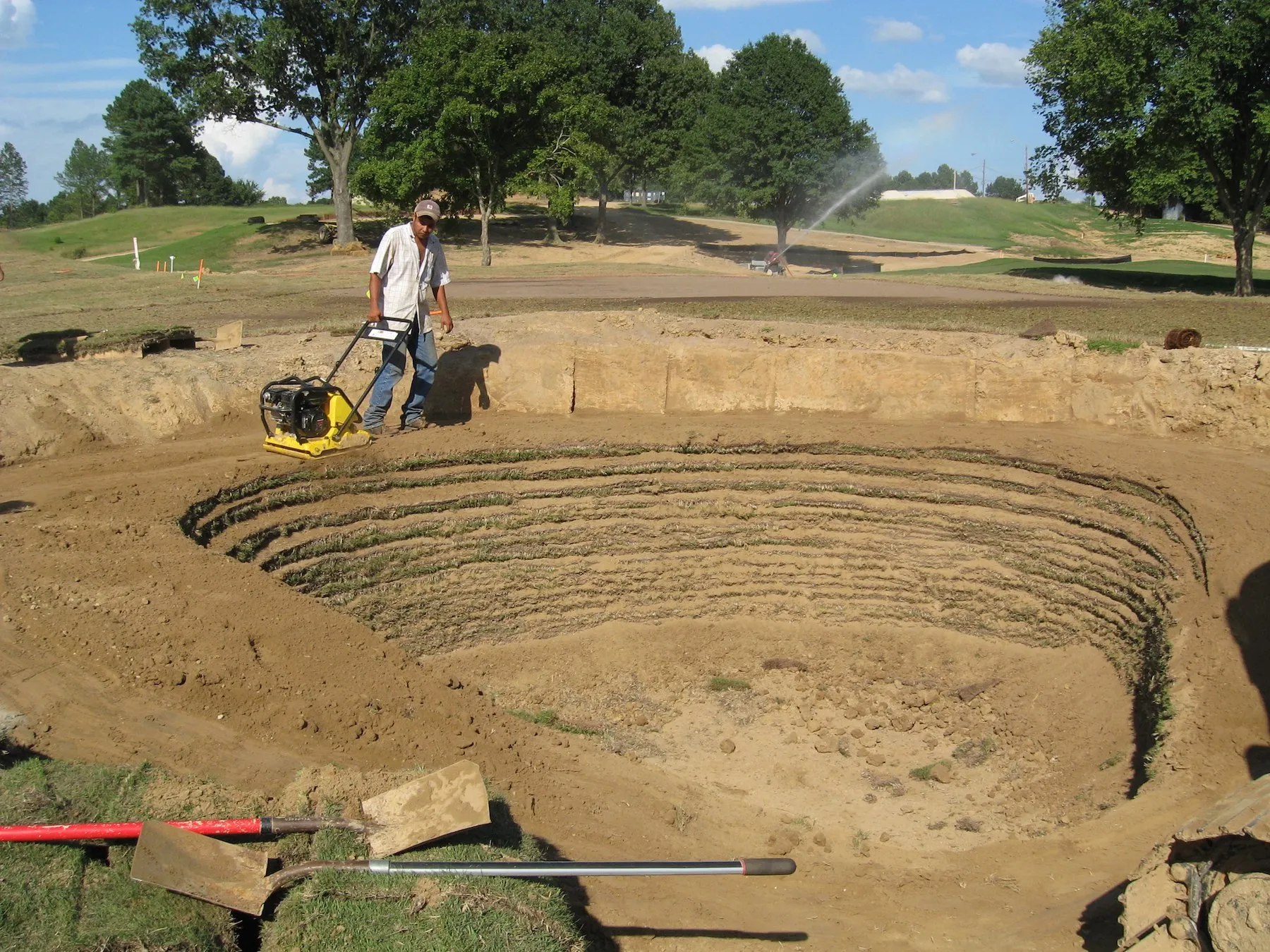 A worker runs a plate compactor around the terraced base of a new bunker at Mirimichi.