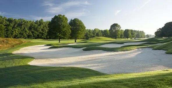 A long white sand bunker sweeping along the edge of a fairway on a clear day.